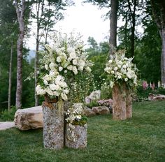 three wooden vases filled with white flowers sitting on top of a lush green field