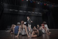 a group of young people sitting on the floor in front of a stage with lights