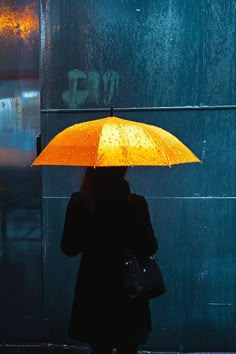 a woman holding an orange umbrella in the rain on a city street with graffiti behind her