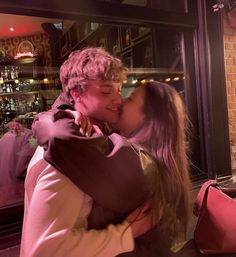 a young man and woman kissing in front of a window with pink lights behind them