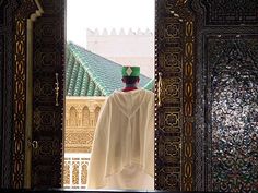 a man in a white robe and green hat standing at the entrance to a building