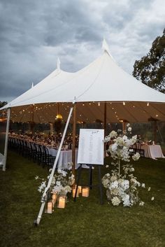 a large tent with candles and flowers on the grass at an outdoor wedding reception under a cloudy sky