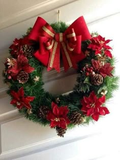 a wreath hanging on the front door with poinsettis, pine cones and bows