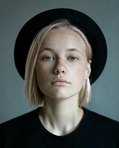 a woman with blonde hair wearing a black hat and looking off to the side while standing in front of a gray background