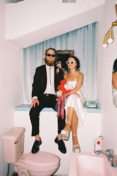 a man and woman sitting on top of a toilet in a bathroom next to each other