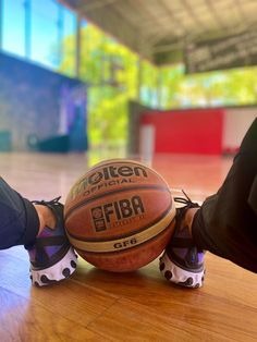 a basketball sitting on top of a wooden table next to a pair of feet wearing sneakers