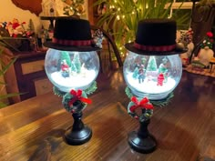 two snow globes sitting on top of a wooden table with christmas decorations in them