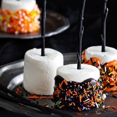 three marshmallows with sprinkles and black sticks sticking out of them