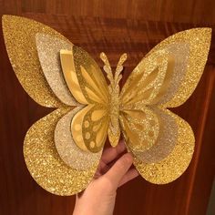 a hand holding up a golden butterfly with gold glitters on it's wings