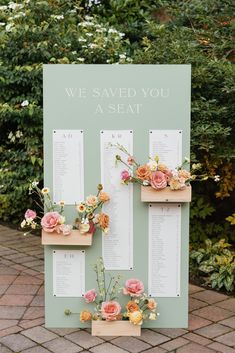 an outdoor seating arrangement with flowers and seating cards on the side of a green sign