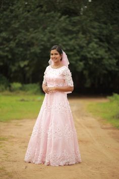 a woman in a pink wedding dress standing on a dirt road with trees in the background