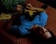 a man laying on top of a bed holding a guitar