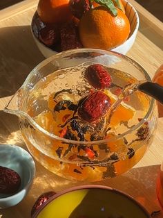 oranges, cherries and other fruit are in bowls on a wooden table top