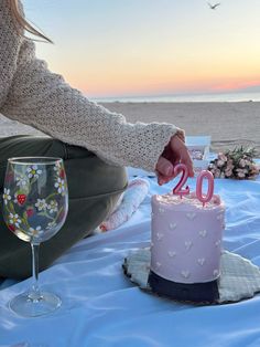 a woman sitting on the beach with a cake and wine glass in front of her