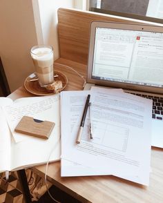 a laptop computer sitting on top of a wooden desk next to a cup of coffee