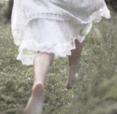 a woman in a white dress is walking through the grass