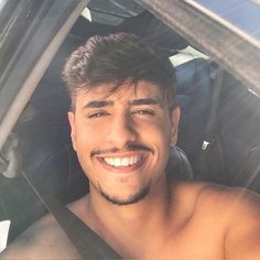 a shirtless man sitting in the back seat of a car smiling at the camera