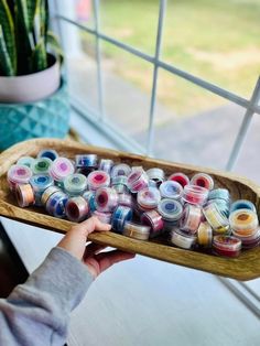 a person holding a wooden tray filled with lots of spools of colored thread