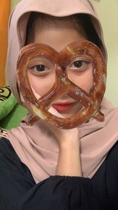 a woman wearing a scarf holding up a pretzel mask