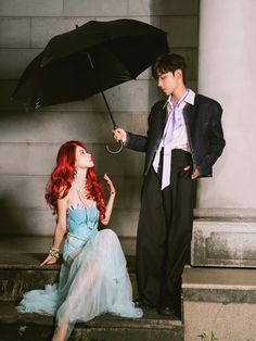 a man holding an umbrella next to a woman in a blue dress sitting on steps