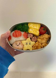 a person holding a metal bowl filled with different types of sushi and other foods