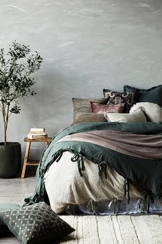 a bed with green sheets and pillows next to a potted plant on a table