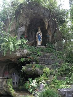 a statue in the middle of a garden with trees and plants around it, surrounded by greenery