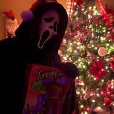 a person wearing a mask and holding a box in front of a christmas tree