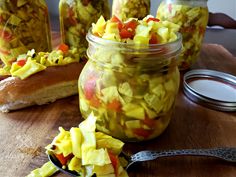 pickled vegetables in jars with spoons on wooden table next to canister and utensils