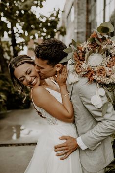 a bride and groom kissing in front of a building with greenery on the side