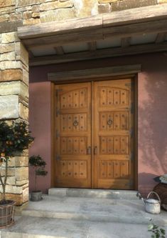 two large wooden doors are on the side of a building with potted plants in front of it