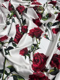 a white and red rose print fabric with green leaves on the bottom half of it