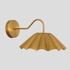 a brass wall light with an arm and shade on the side, against a gray background