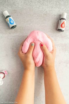 a person holding a pink doughnut on top of a white table next to other items