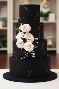 a three tiered black cake with white flowers on it