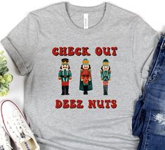 "Looking for a funny Christmas shirt that will make you the life of the party? Look no further than Deez Nuts! This hilarious t-shirt features colorful nutcrackers standing in a line with festive red and green outfits. Plus, the slogan \"check out deez nuts\" is sure to get a laugh from anyone who sees it. So put on your jolly best and order Deez Nuts funny Christmas shirt today! Soft cotton and quality print make users fall in love with it over and over again. These t-shirts have-ribbed knit co Funny Christmas Shirts Zazzle, Funny Xmas Tshirts, Christmas Tees Funny, Funny Christmas Shirts Hilarious, Christmas Shirt Ideas Funny, Friend Christmas Party, Funny Christmas Pajamas, Funny Christmas T Shirts, Funny Holidays