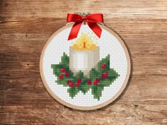 a cross stitch christmas ornament hanging on a wooden wall with a red bow