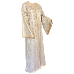 Elegant Moroccan caftan white and gold lame metallic floral brocade kaftan.Circa 1970s.This beautiful long dress is hand crafted in Morocco and tailored for a relaxed fit with wide sleevesThis long maxi dress vintage kaftan is embroidered and embellished entirely by hand.One of a kind evening Moroccan Middle Eastern gown.The kaftan features a traditional neckline, embellished princess bell sleeves.It is a slip on, the button does not open.In Morocco, fashion preserves its traditional style inher Brocade Kaftan, Vintage Kaftan, Moroccan Fabric, Vintage Dress Design, Bohemian Fabric, Beautiful Long Dresses, Moroccan Kaftan, Moroccan Fashion, Gold Lame