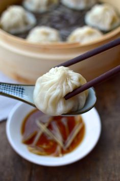 dumplings with chopsticks are being held up over a bowl of dipping sauce