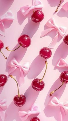 cherries with pink bows are arranged on a pink surface