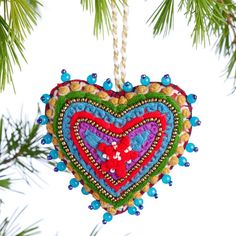 a heart shaped ornament hanging from a pine tree with beaded decorations on it