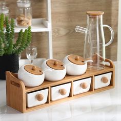 three white dishes are sitting on a wooden tray next to a glass pitcher and potted plant