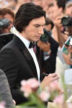 a man in a tuxedo looking at his cell phone while surrounded by photographers