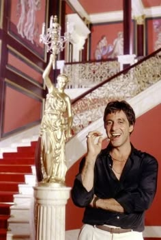 a man standing next to a golden statue on top of a stair case in front of a red wall