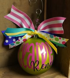 a green ornament with pink, yellow and blue ribbon hanging from it's side