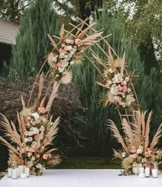 an arch decorated with flowers and candles stands in front of tall grass, bushes and trees