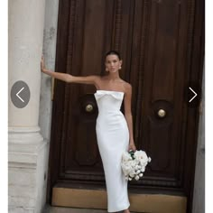 a woman standing in front of a door wearing a white dress and holding her arm out