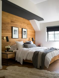 a bedroom with wood paneled walls and white bedding, along with two framed pictures on the wall