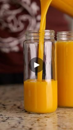 a person pouring orange juice into two glass jars