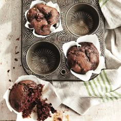 chocolate muffins in paper cups sitting on a baking tray next to a napkin